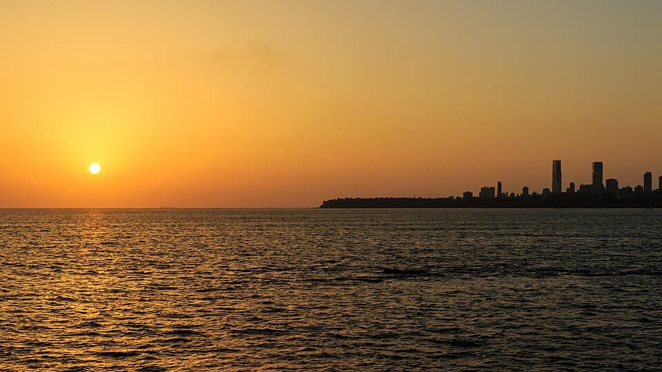 The Mumbai skyline in silhouette as the sun sets over Marine Drive and the Arabian Sea.